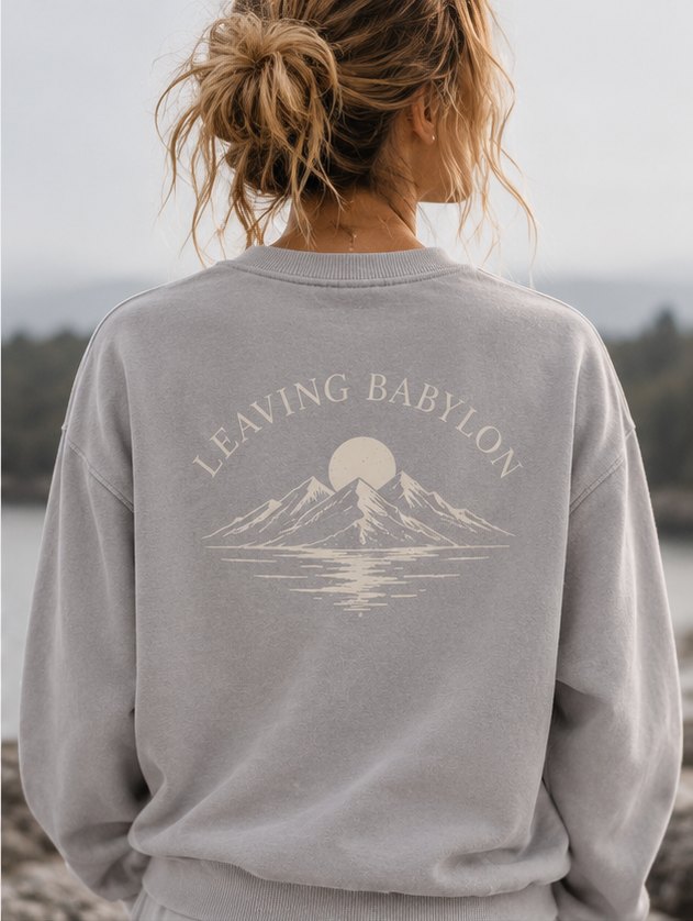 Woman by a lake in the grey Zion Finder crewneck: Leaving Babylon arched over a sun, mountains and water across the back